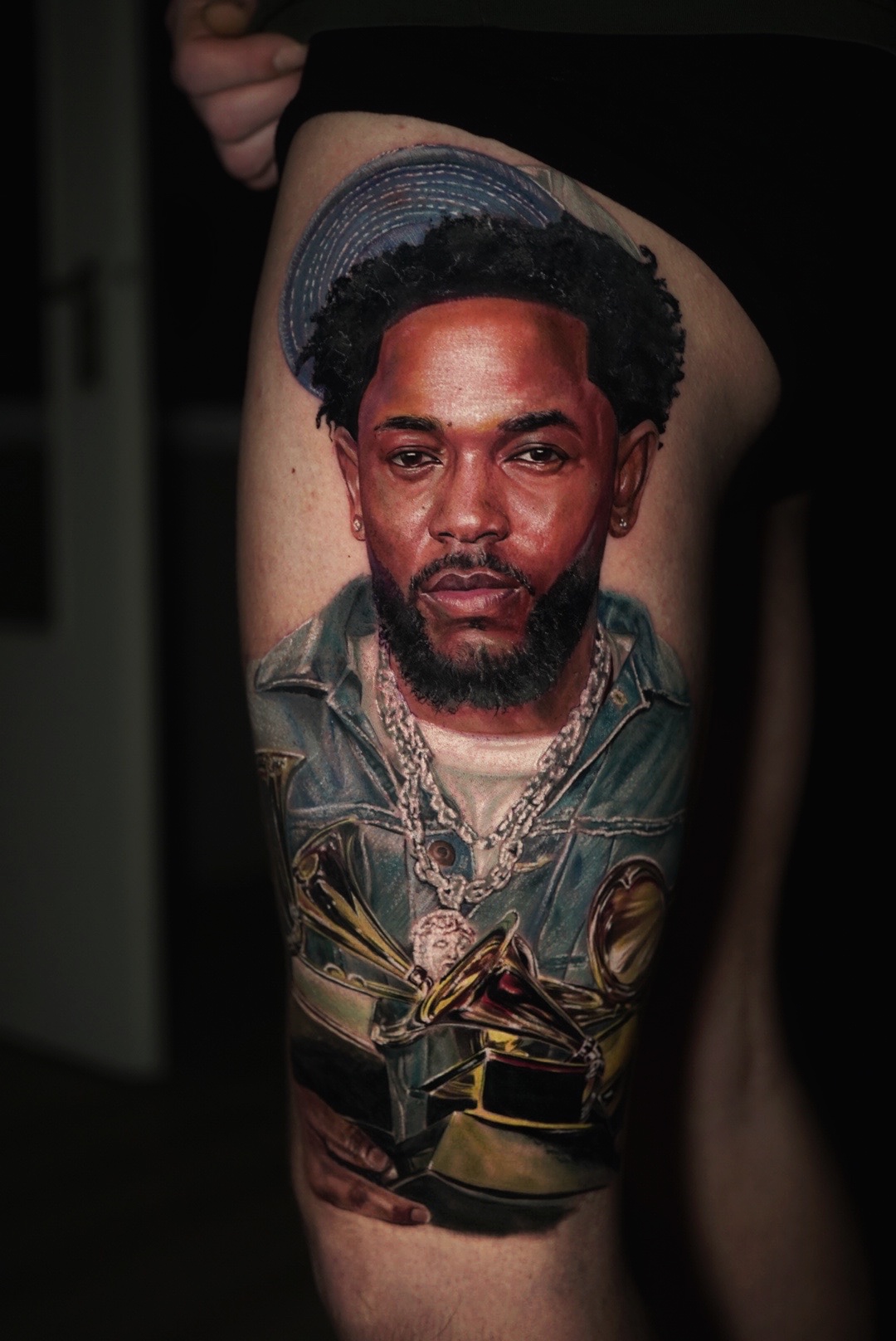 Color realism tattoo of a rapper with an album cover and awards on a thigh